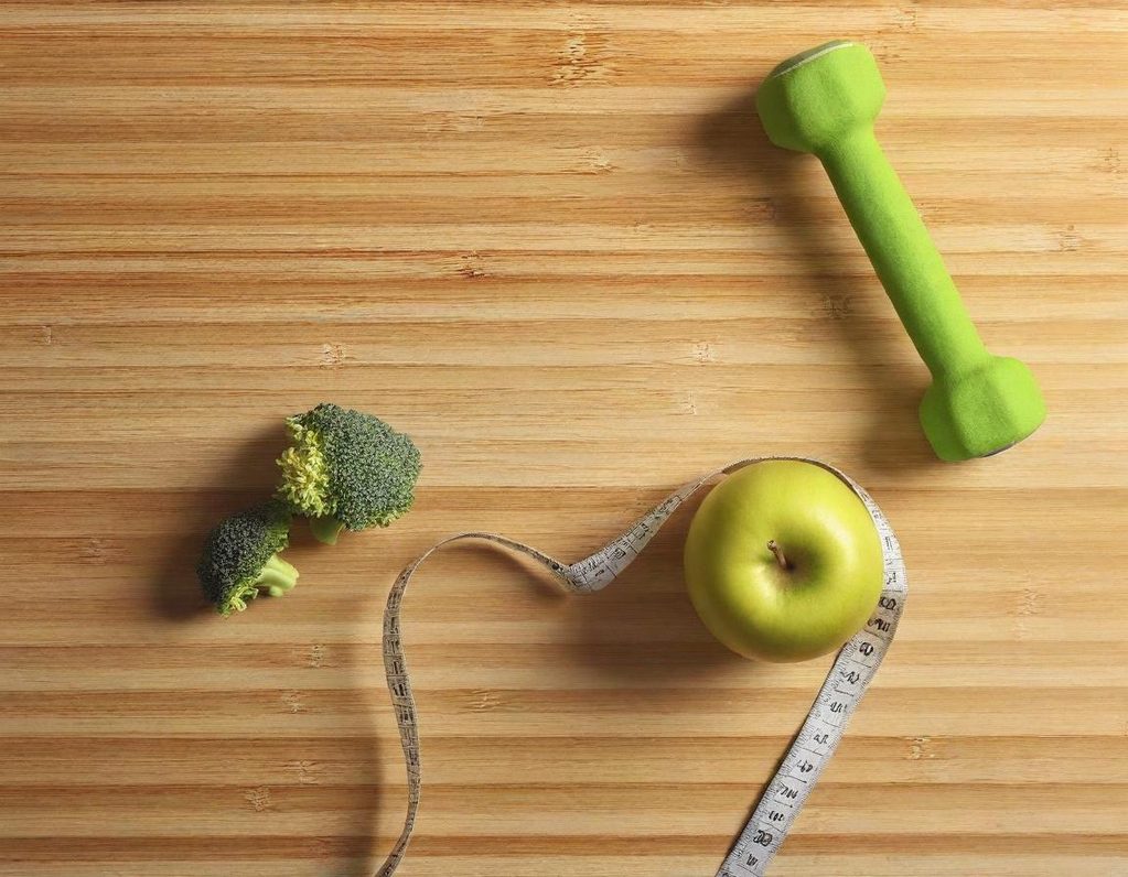 no tengas miedo al cambio Una pesa verde, brócoli, una manzana y una cinta métrica sobre una superficie de madera.