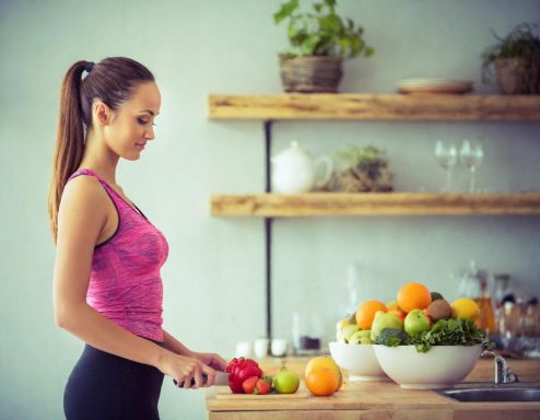 Mujer en cocina con frutas frescas, cortando una manzana sobre la mesa.